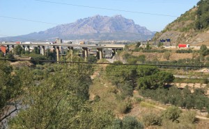 Pista para carros, linha de trem e trilha ao longo do rio. No fundo as montanhas de Montserrat