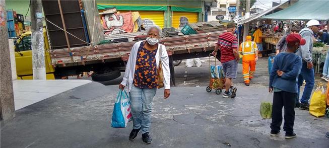 Senhora idosa carrega sacolas em uma feira de São